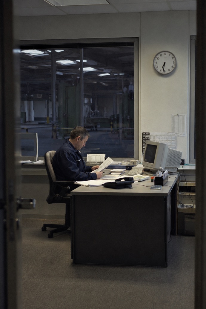 An employee sits at their desk early in the morning overlooking the production hall, reading documents