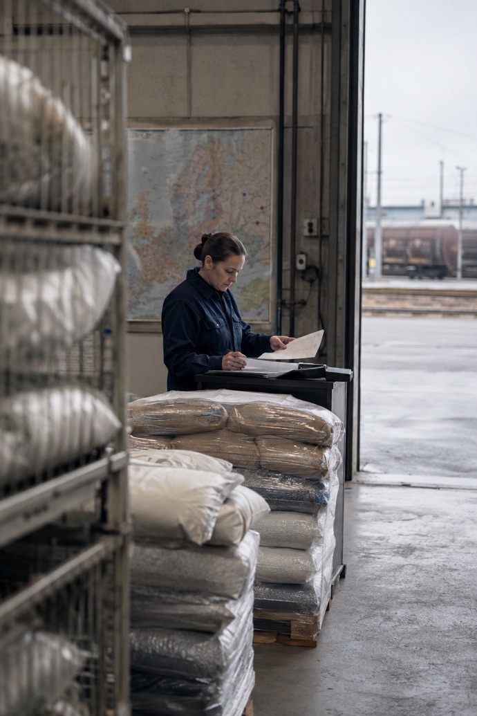 An employee checks a delivery list against palletised bagged goods at a warehouse goods-receiving area
